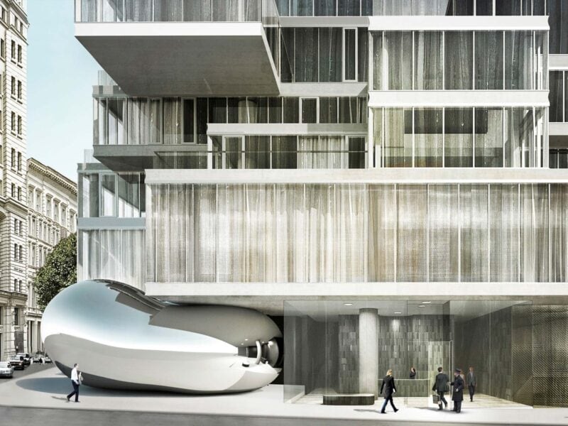 A modern office building with sleek glass architecture and a sculpture of a reflective bean below the office.
